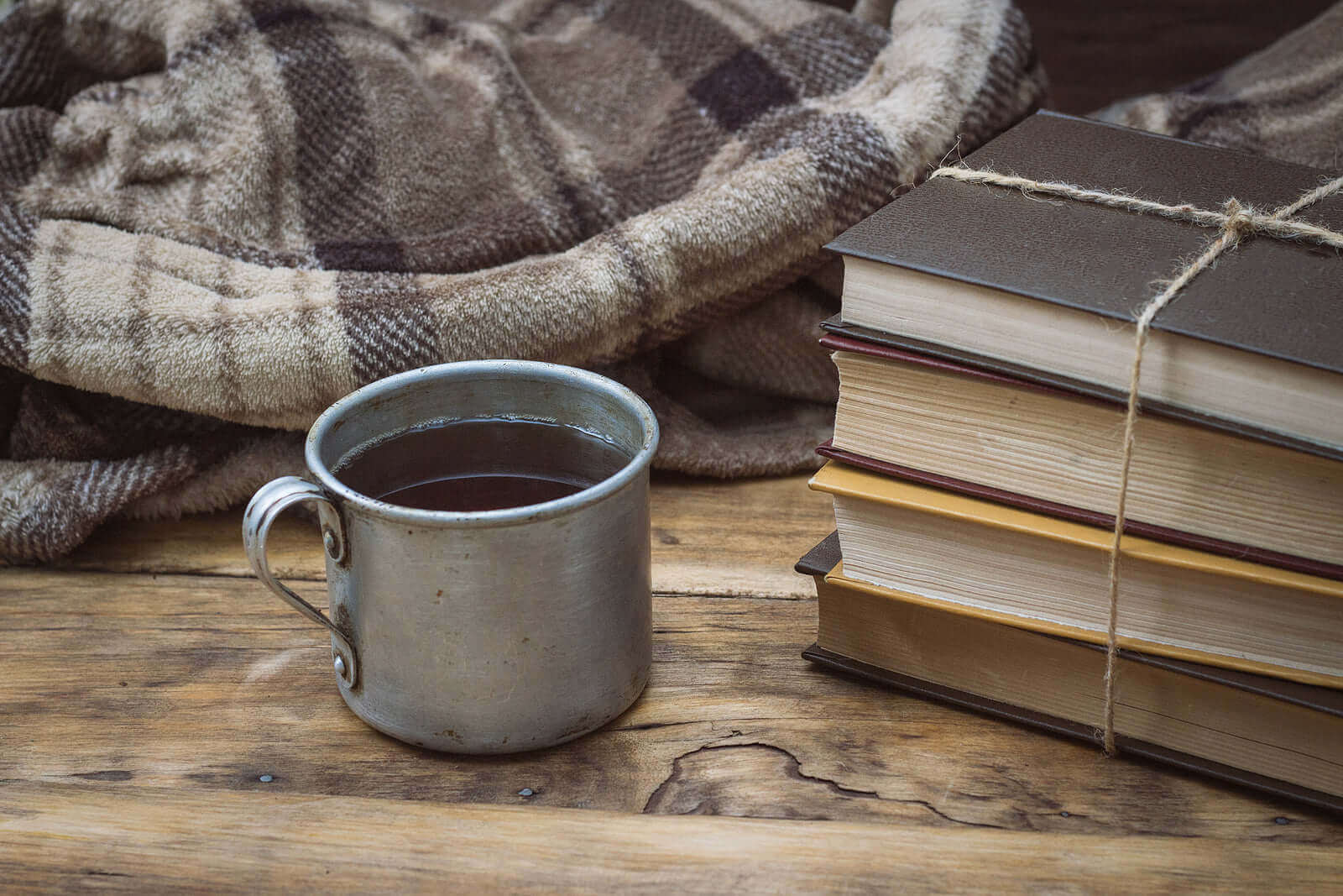 Cozy scene featuring a rustic mug of coffee beside stacked books on a wooden table and a soft blanket.