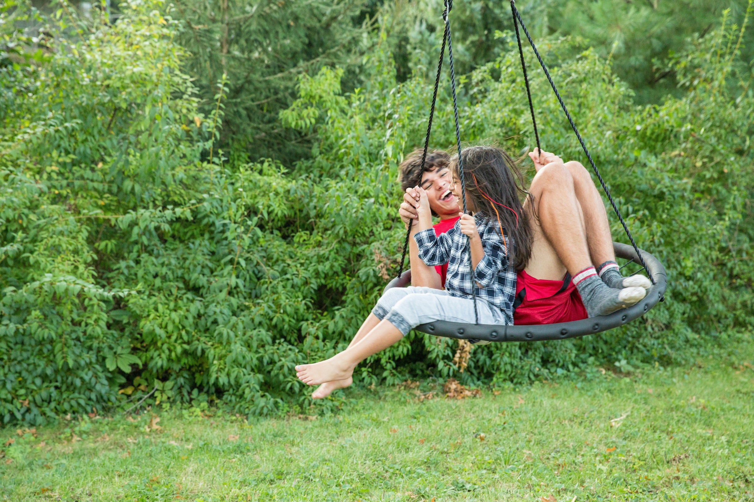 Children enjoying an affordable outdoor swing in a lush green backyard setting, showcasing quality playtime fun.