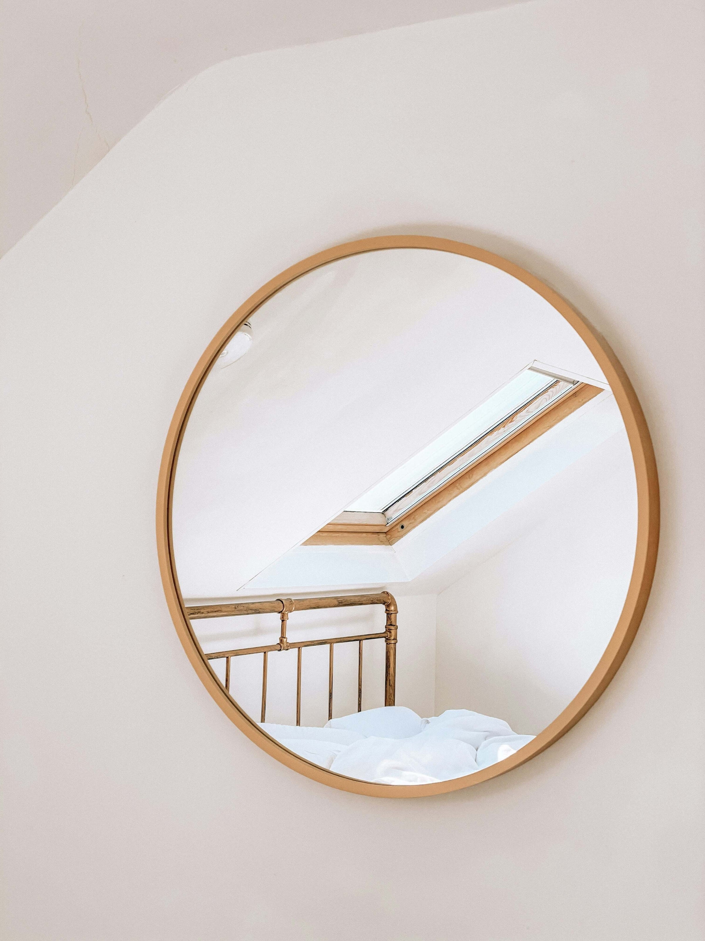 Round wall mirror reflecting a skylight and bed frame, adding affordable style and elegance to your room on a budget.