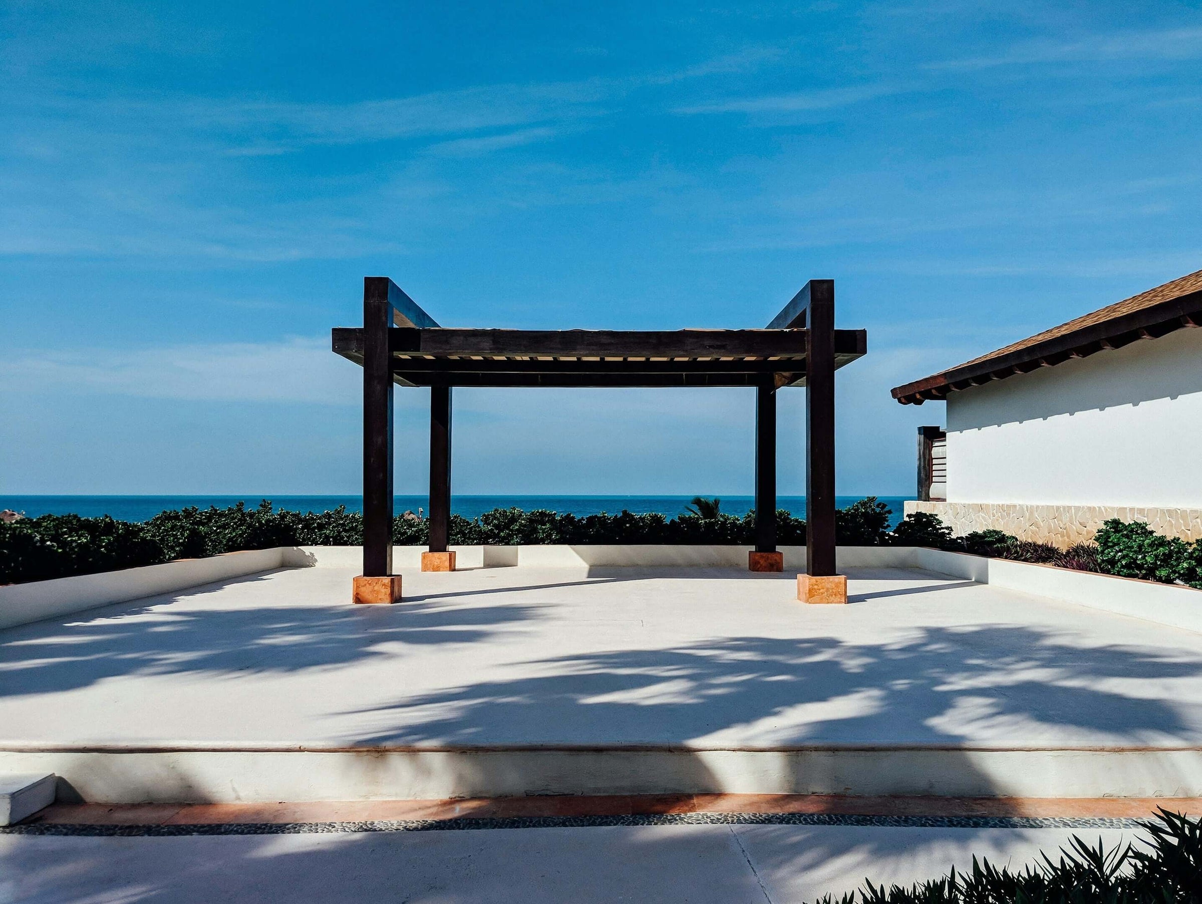 Stylish wooden pergola providing shade in a modern patio setting with ocean view, ideal for affordable outdoor living enhancement.