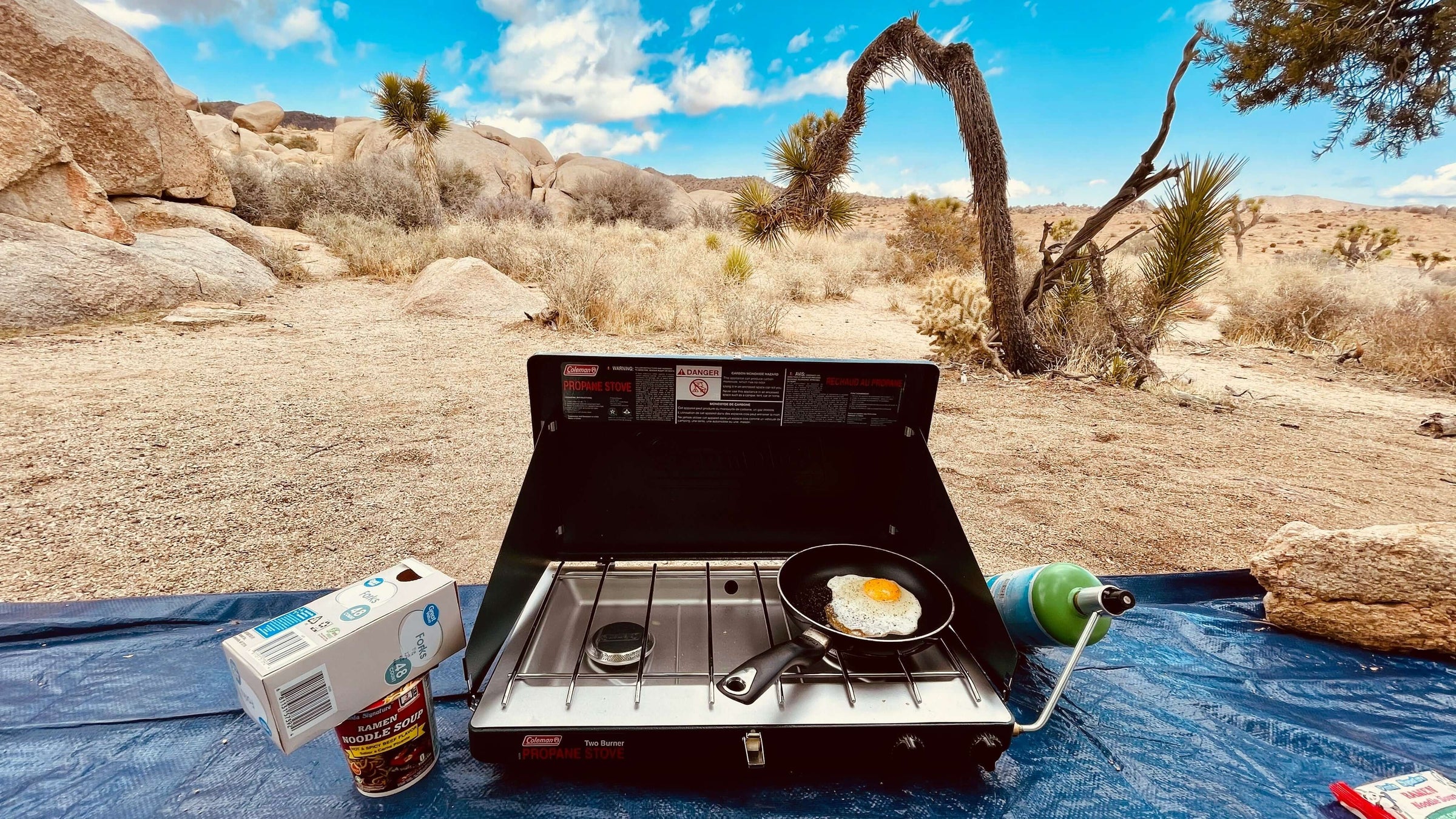 Outdoor camping stove with frying pan cooking eggs, set in a rocky desert landscape.