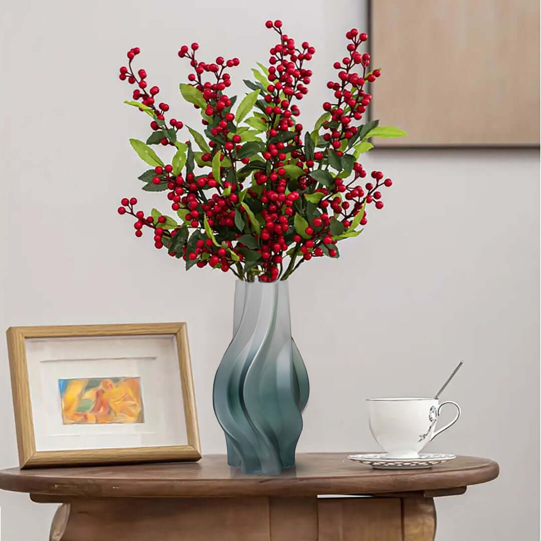 Stylish home décor featuring a vase with red berry branches on a wooden table alongside a framed picture and teacup.