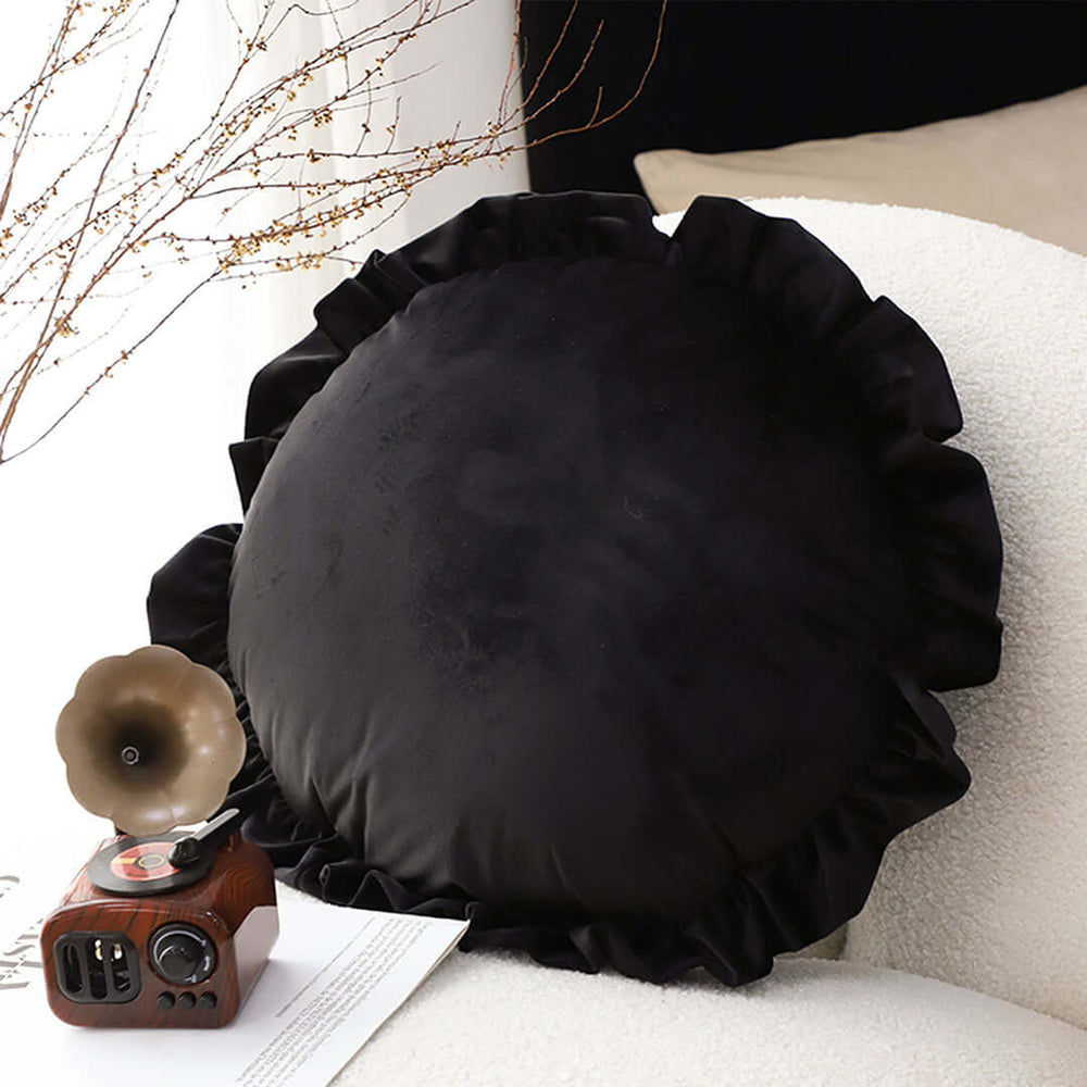 Affordable high-quality black round cushion with ruffled edges beside vintage-style radio on a white textured chair for value furniture seekers.