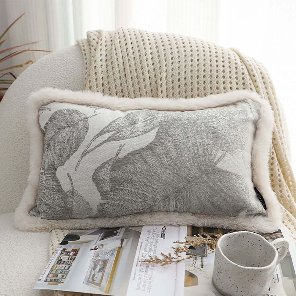 Gray decorative pillow with a leaf pattern and faux fur edge, placed on a cozy chair with a blanket, showcasing quality, affordable homewares.