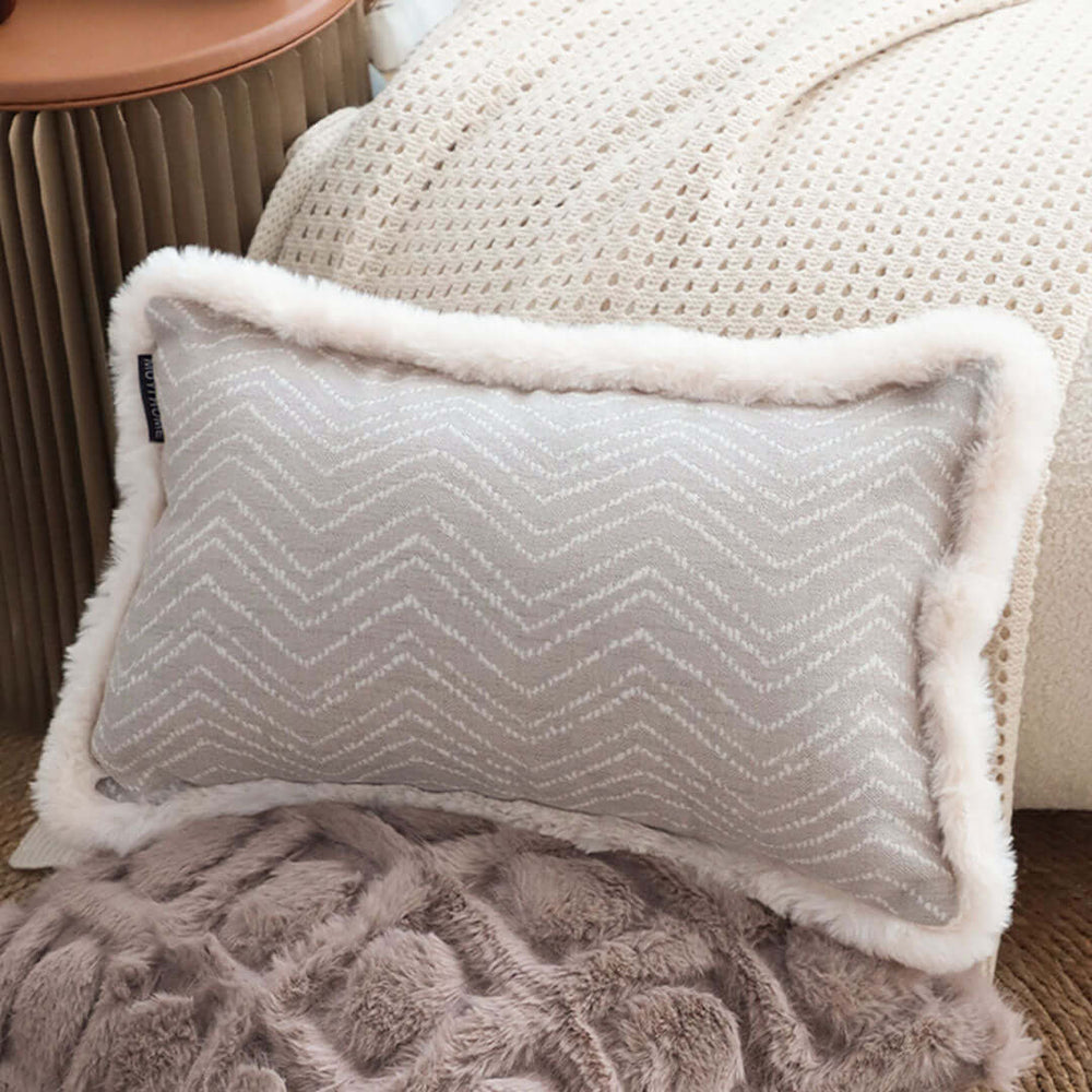 Affordable quality homewares - cozy grey cushion with textured pattern and soft faux fur edges on a beige knitted blanket.