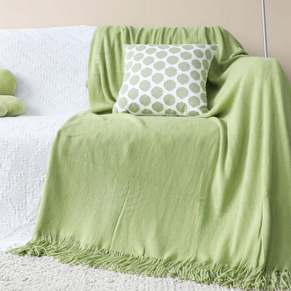 Cozy living room setting with a green throw blanket and patterned pillow on a white couch, showcasing affordable and quality homewares