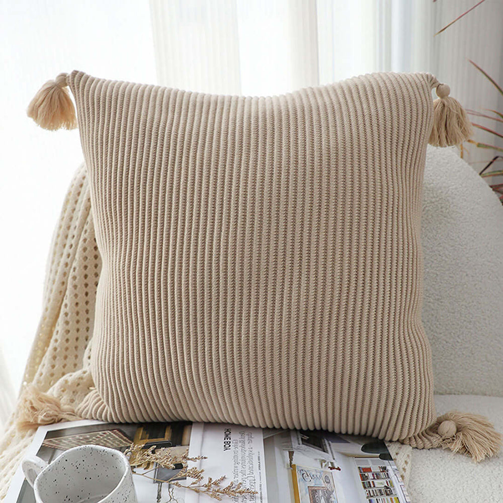 Affordable quality homewares - ribbed beige cushion with tassels on a cozy white chair next to a blanket and magazines.