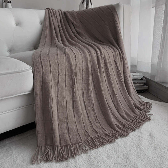 Taupe knitted throw blanket draped over white couch in cozy living room setting