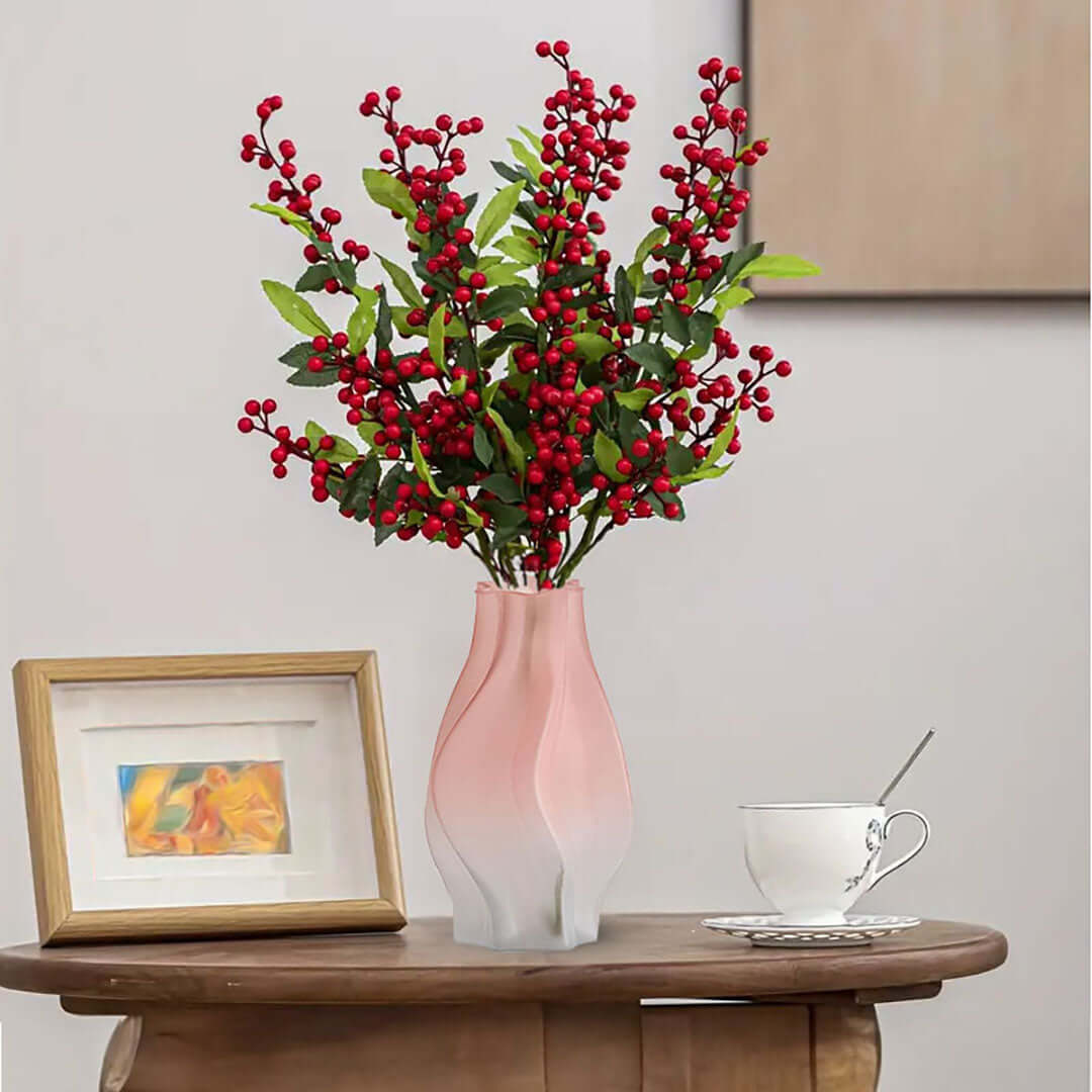 Affordable quality homewares - pink vase with red berries on a wooden table next to a framed picture and a white teacup.