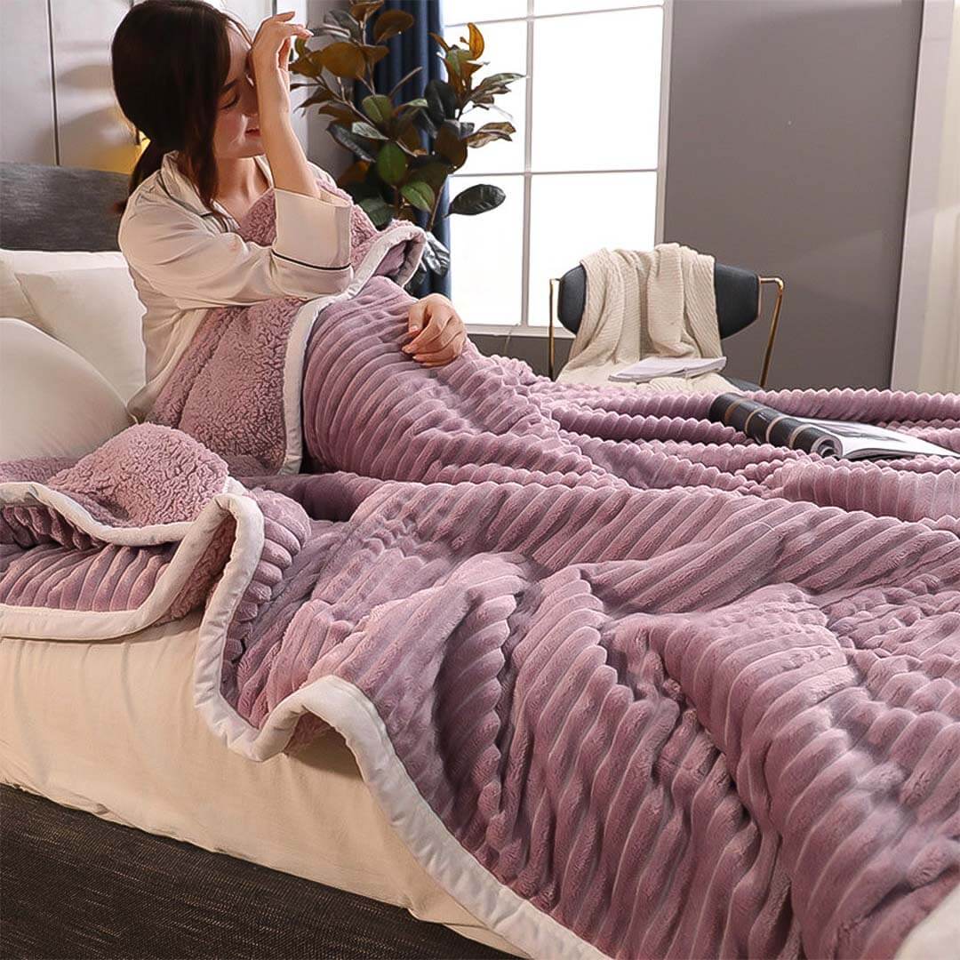 Woman relaxing in bed under a cozy, purple textured blanket in a stylish bedroom setting.