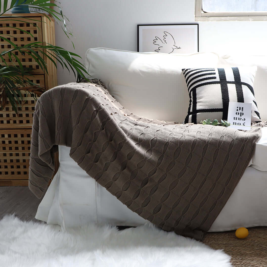 Affordable quality homewares - stylish value furniture with a cozy brown knit blanket on white sofa, decorative cushion, and green plant.