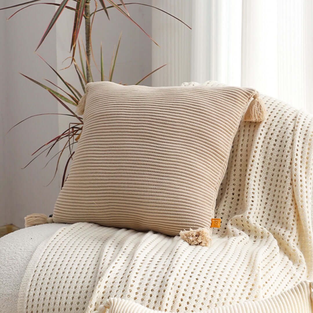 Beige decorative pillow on cozy white knitted blanket, showcasing affordable homewares with quality and value furniture elements.