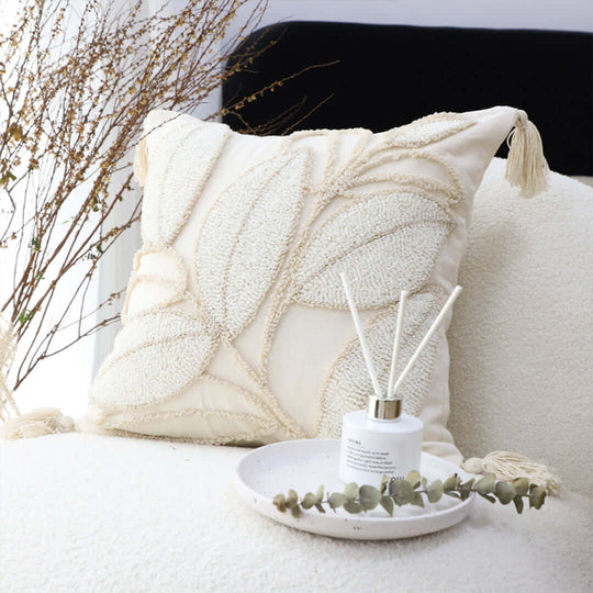 Affordable quality homewares featuring a decorative pillow with leaf designs and a reed diffuser on a cozy white chair