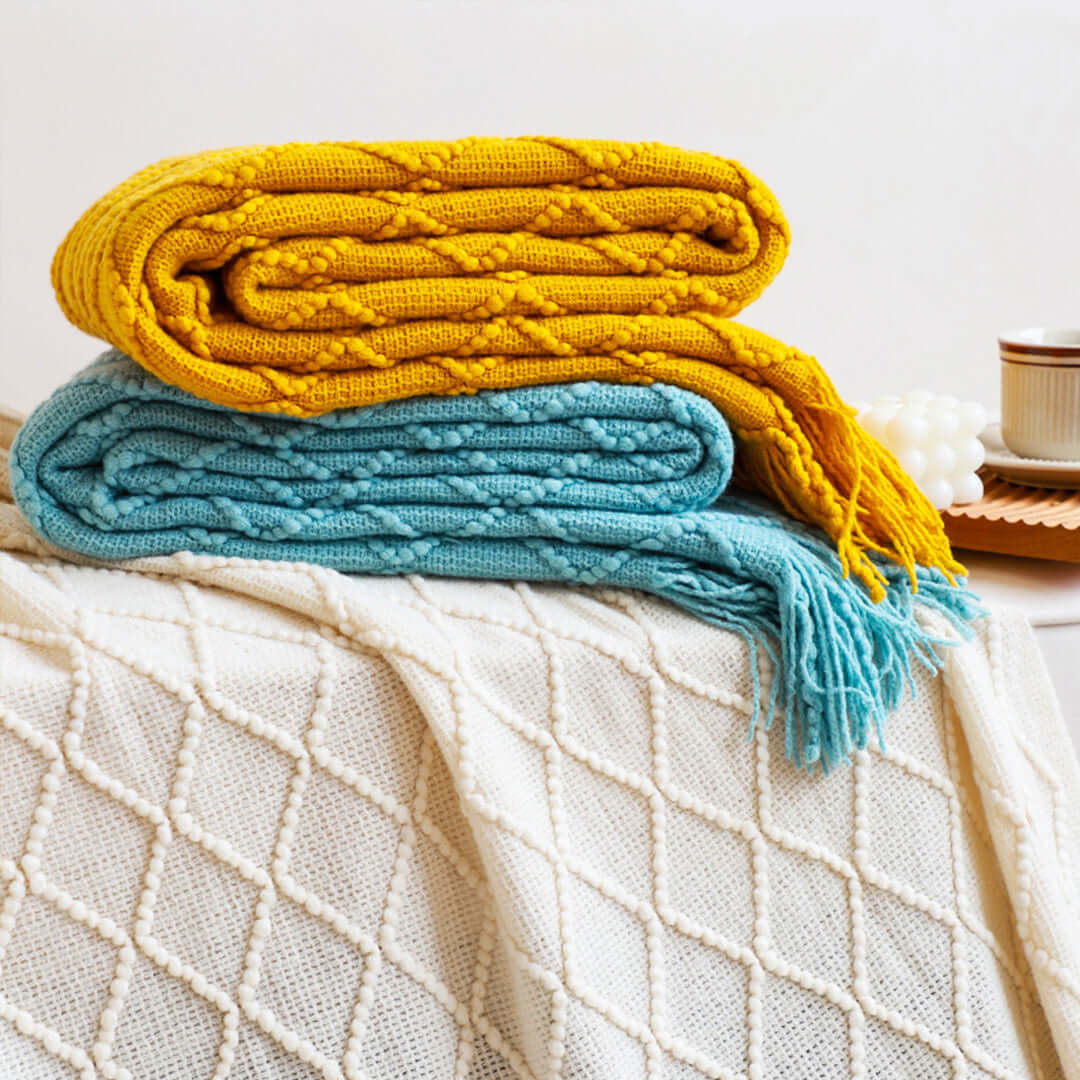 Affordable quality homewares - Yellow and blue knitted blankets on a textured white throw blanket exemplify value furniture.