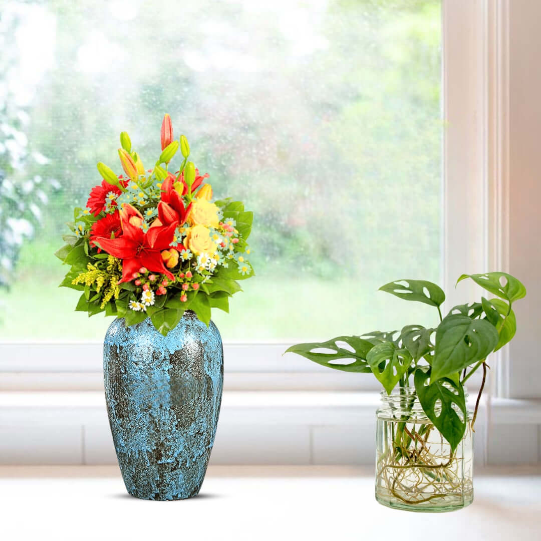 Vibrant flower arrangement in a blue vase next to a potted plant on a windowsill