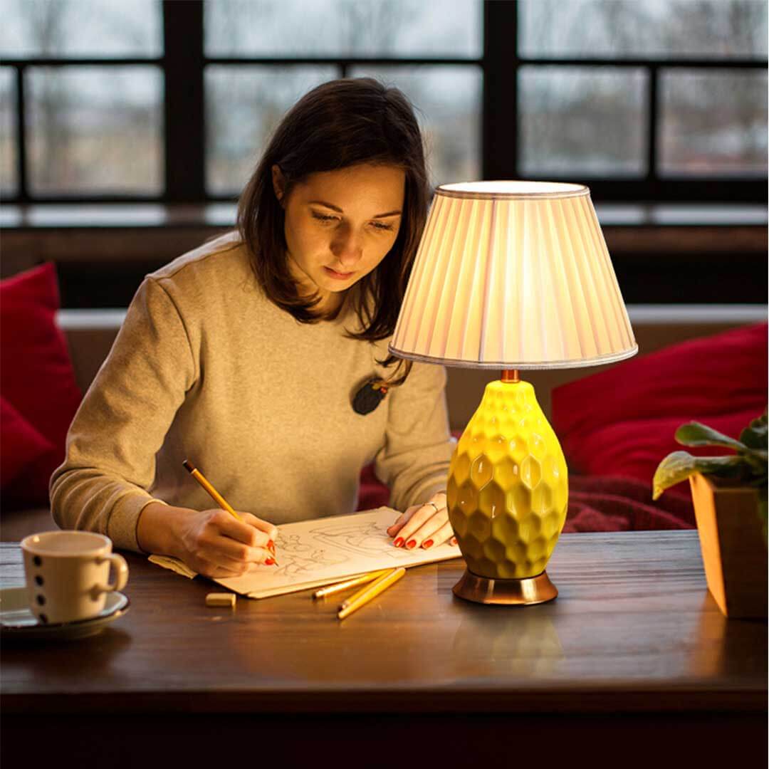 Woman working at table with affordable quality homeware, including a stylish yellow lamp, reflecting value furniture in cozy setting