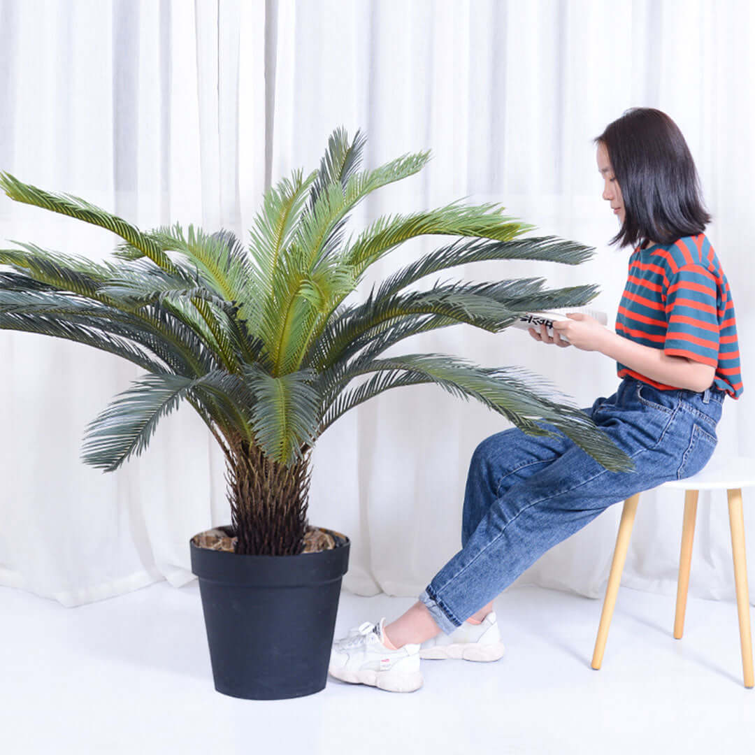 Woman sitting on stool beside large potted plant in modern home setting