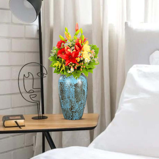 Decorative blue vase with colorful flowers on a wooden bedside table next to a bed in a cozy home setting