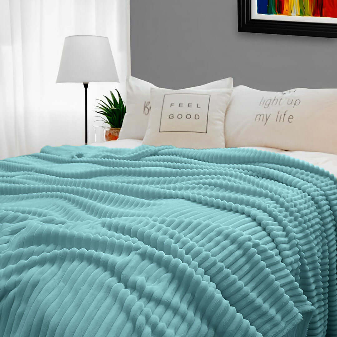 Cozy bedroom featuring a light turquoise ribbed blanket on a bed with decorative pillows, modern lamp, and plant, offering affordable homewares.