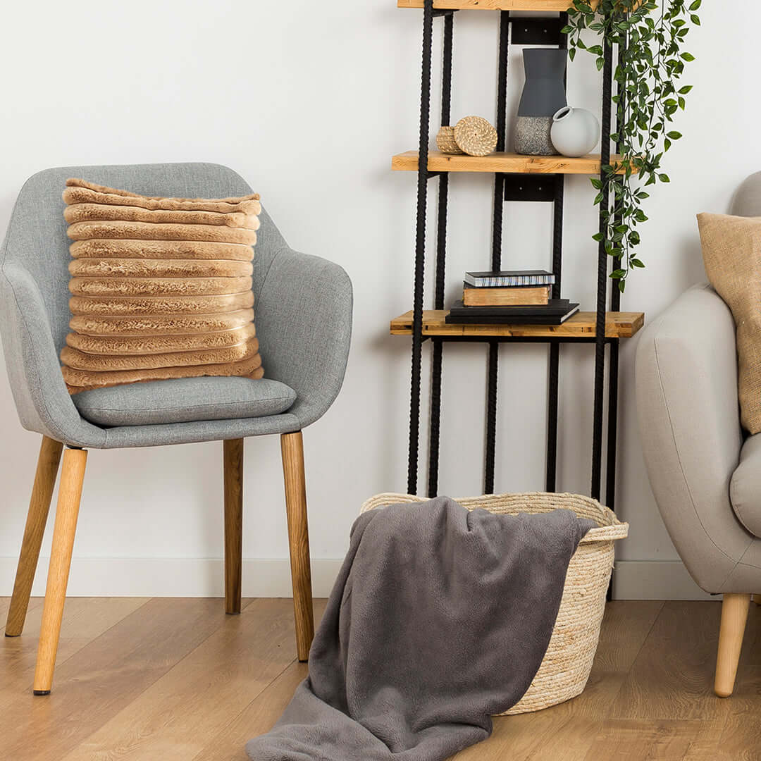 Affordable quality homewares featuring a stylish gray armchair with cushion, cozy basket with blanket, wooden shelf, and decorative plant