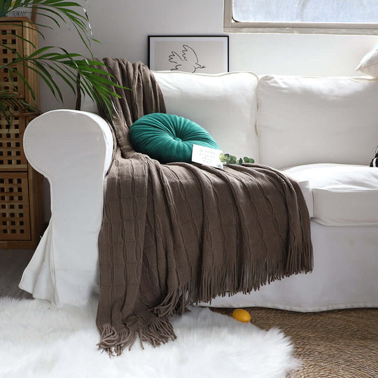 Cozy living room with affordable quality homewares including a white sofa, brown fringed blanket, and green value furniture cushion.