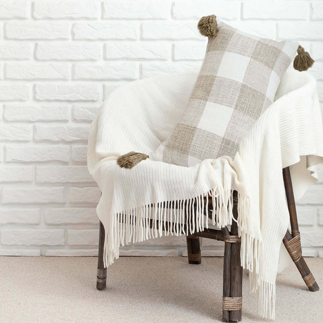 Affordable quality homewares - woven chair with value furniture throw blanket and checkered cushion against white brick wall