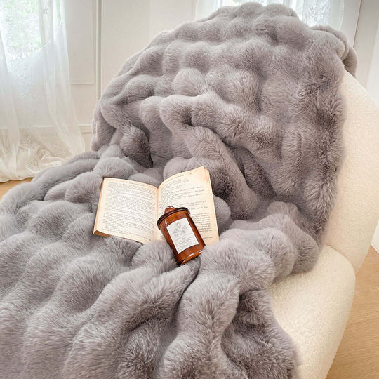 Cozy grey fur blanket on a chair with an open book and a candle, ideal for affordable and quality homewares.