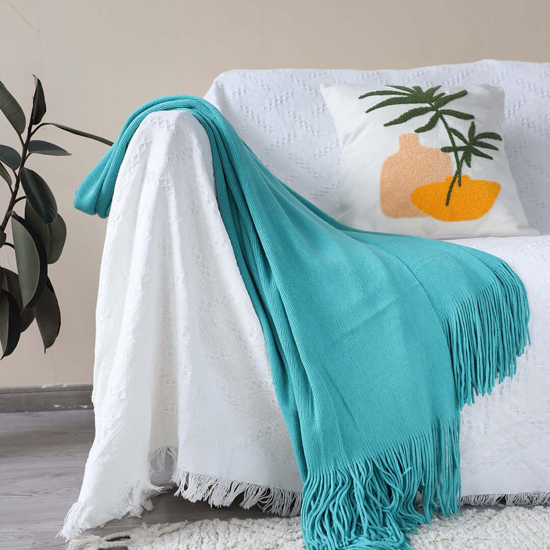 Affordable quality homewares - white sofa with a fringed turquoise blanket and decorative pillow enhancing value furniture.