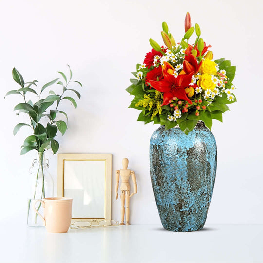 Vibrant floral arrangement in a blue vase on a modern homeware display with a plant, framed picture, and decor items. Affordable quality value furniture.