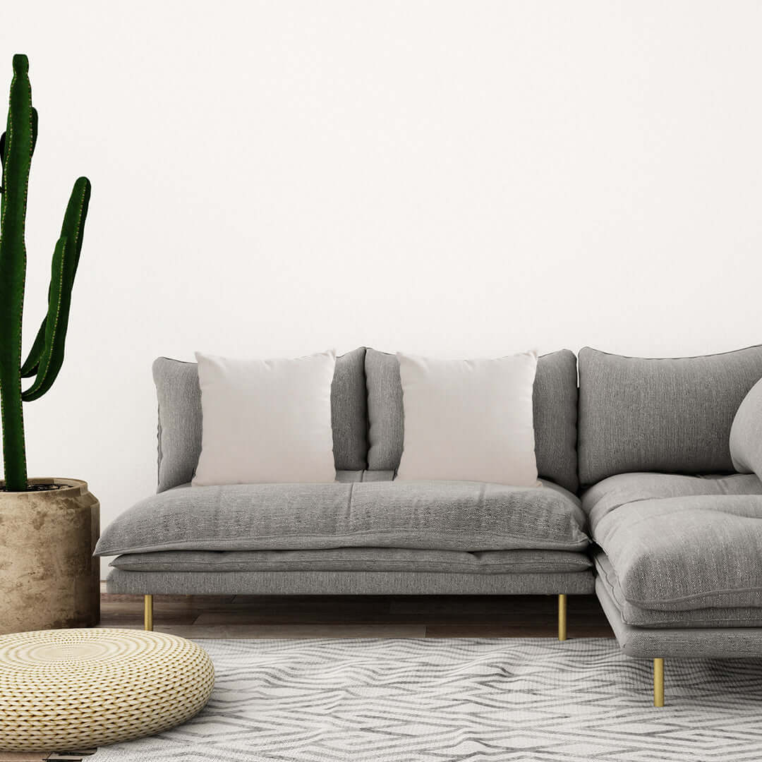 Modern affordable gray sectional sofa with white pillows in a stylish living room with a cactus and woven ottoman, showcasing quality value furniture.