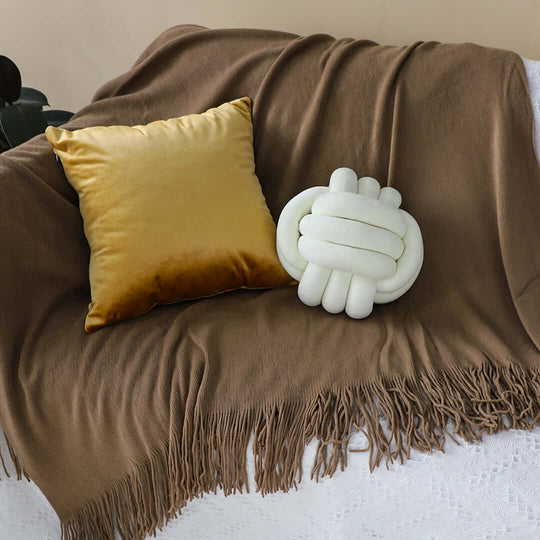 Affordable quality homewares with a cozy brown blanket, mustard yellow pillow, and a unique value furniture knot pillow on display