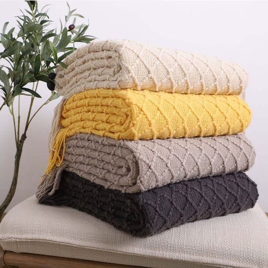 Stack of affordable, quality knitted blankets in various colors on a cushion, offering value homewares and furniture essentials.