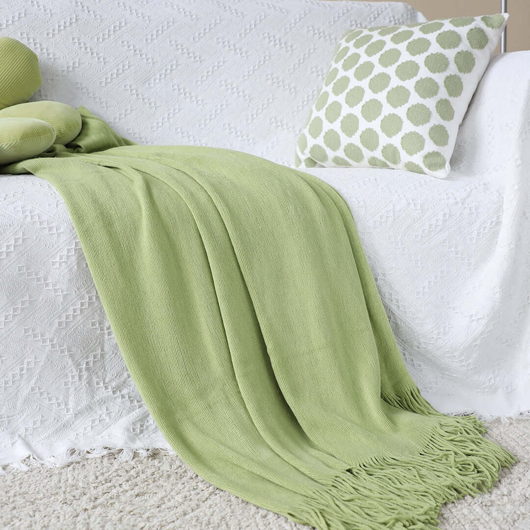 Green throw blanket and patterned pillow on a white sofa, showcasing affordable quality homewares and value furniture.