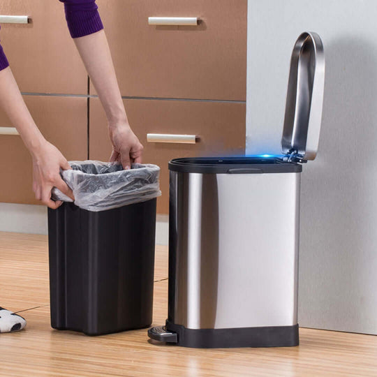 Person changing trash bag in stainless steel kitchen trash can with step pedal in modern home kitchen.