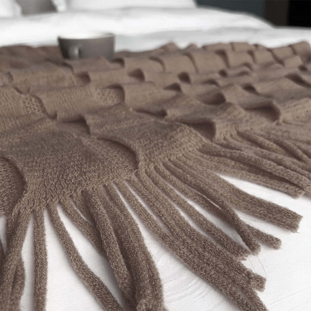 Affordable quality homewares - close-up of a stylish, soft brown throw blanket with tassels spread over a white bed.