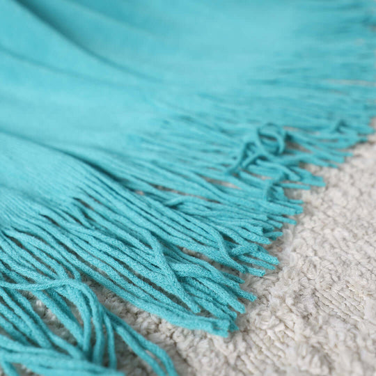 Affordable and quality turquoise fringe blanket on a textured surface, perfect for value homewares and furniture.