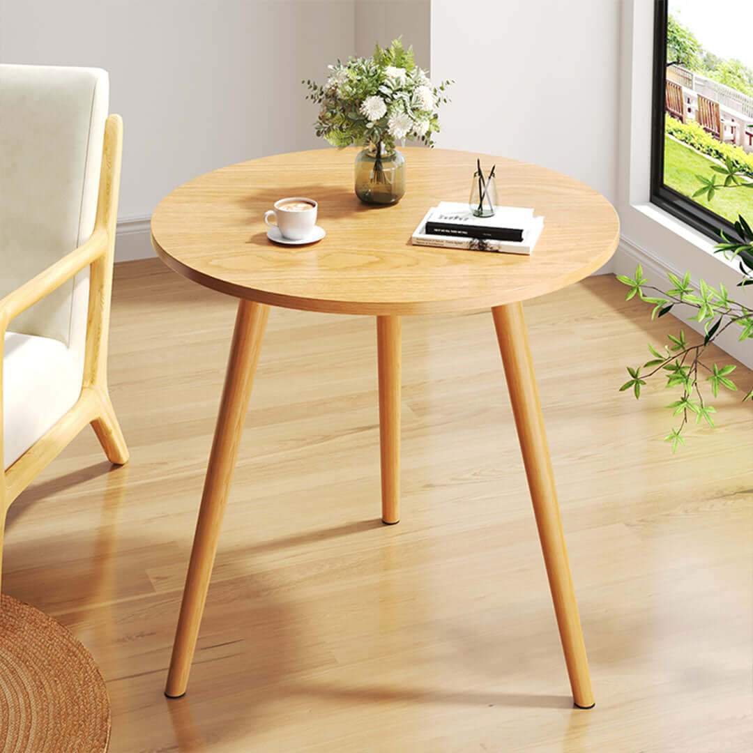 Round wooden table with a cup, a book, and a vase of flowers, next to a chair in a bright room, showcasing affordable quality homewares and value furniture.