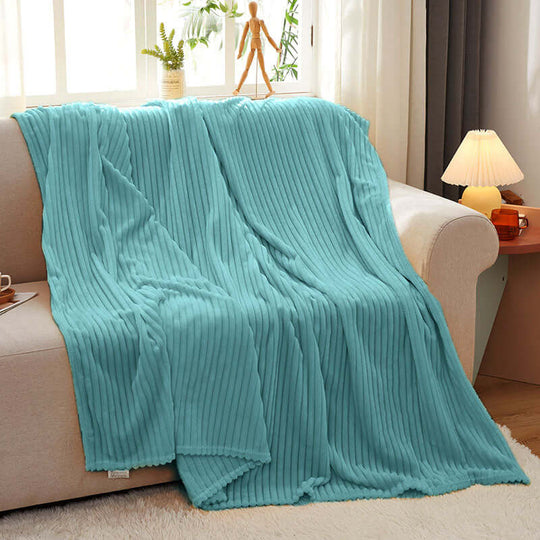 Affordable quality homewares - cozy turquoise blanket draped over a beige sofa in a warmly lit living room.