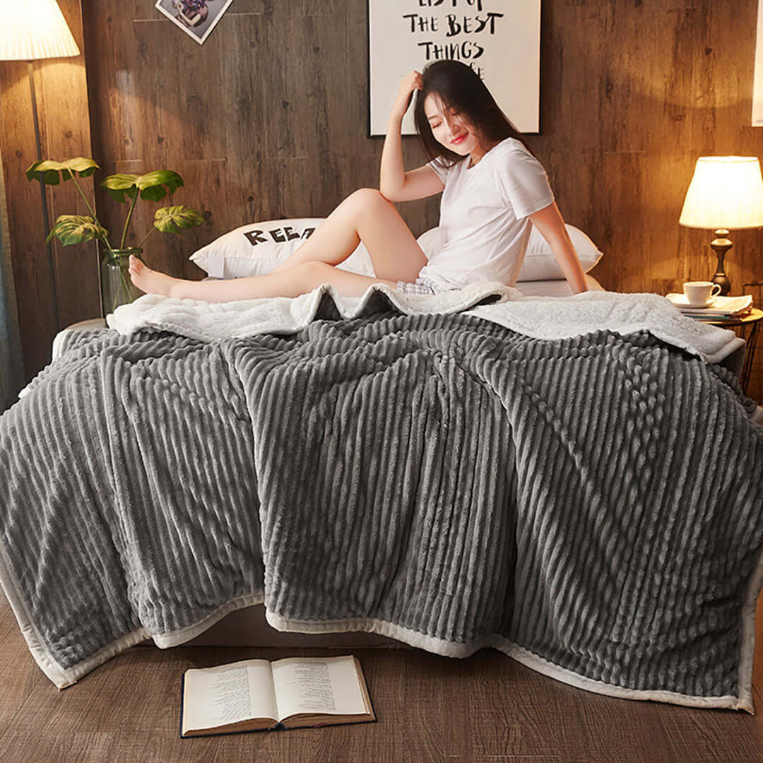 Woman relaxing on bed with cozy grey blanket in ambient-lit room, showcasing affordable and quality homewares and value furniture.