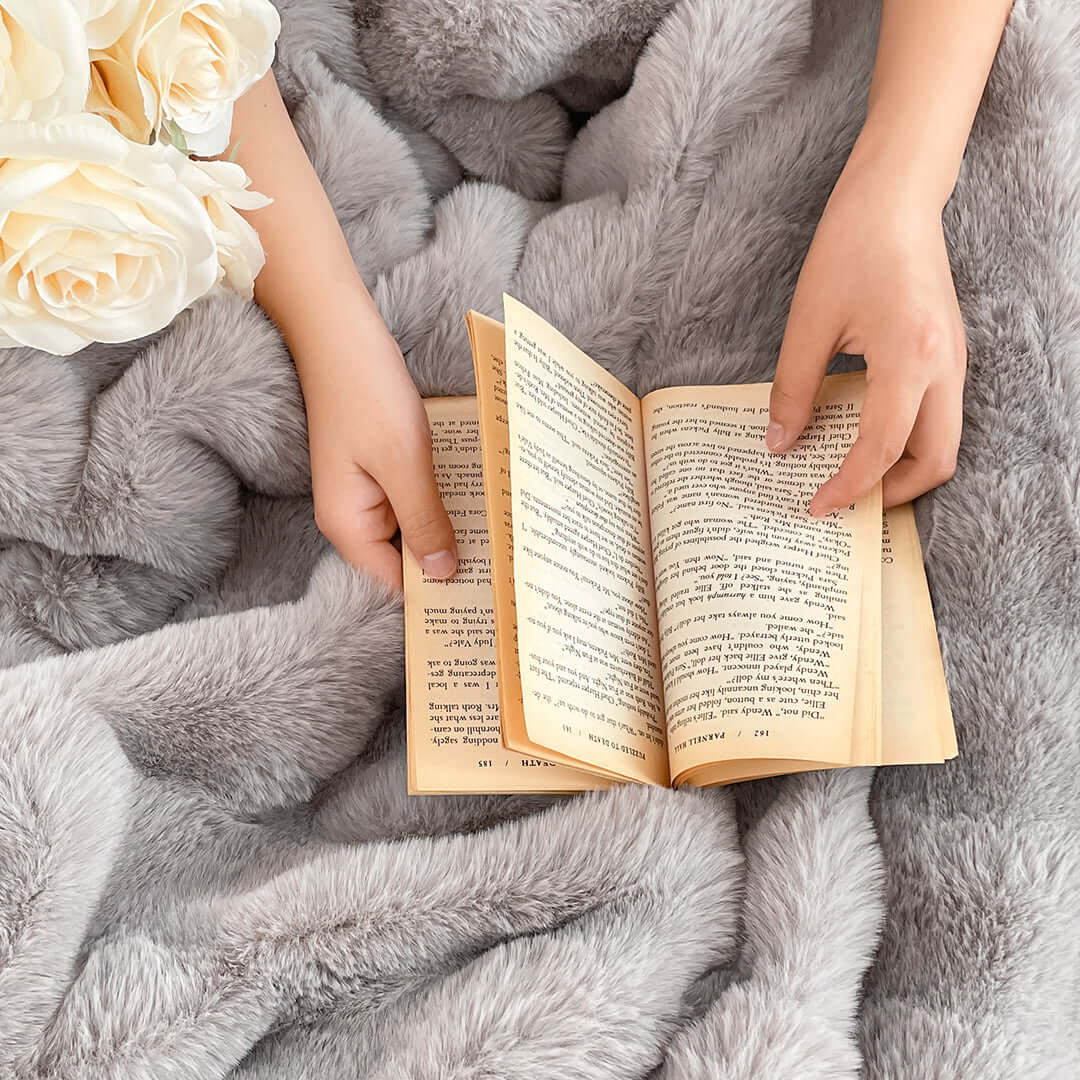 Reading a book on a soft, grey faux fur blanket while holding white roses