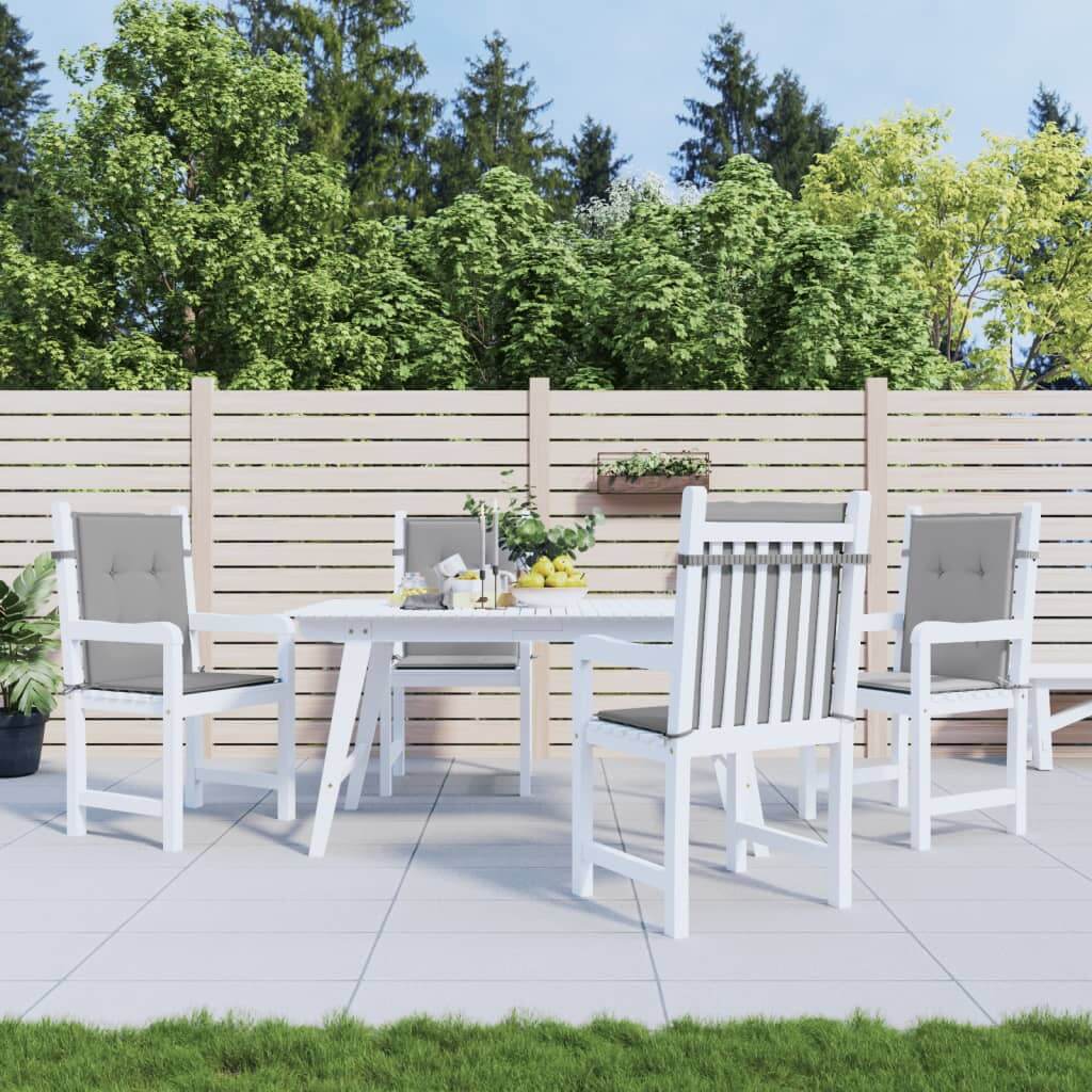 Outdoor dining set with four white chairs and table, featuring grey cushions, set on a patio with lush greenery in the background.