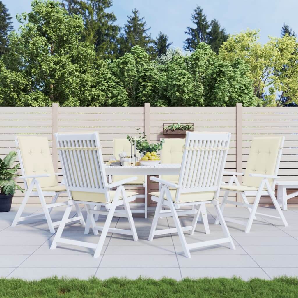 Outdoor patio set with highback chairs featuring cream cushions, surrounded by greenery and a wooden fence.