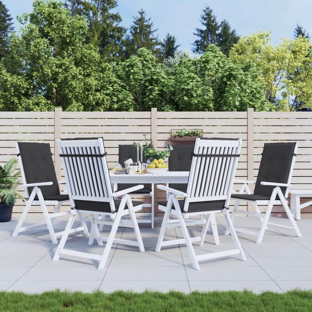 Outdoor patio set with black highback chair cushions on white chairs around a round table, set in a garden with trees and fencing.