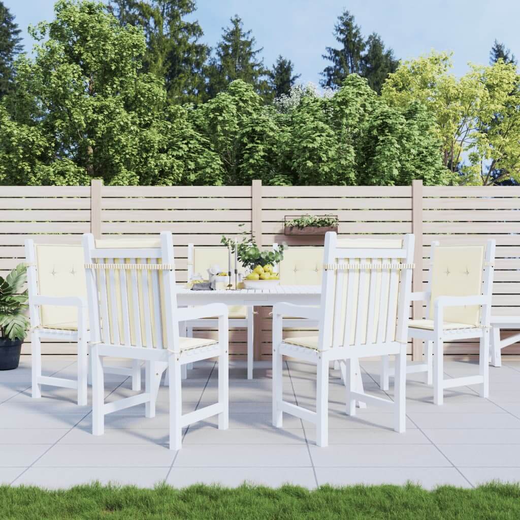 Outdoor patio set with white wooden chairs featuring cream lowback cushions, surrounded by greenery and a wooden fence.