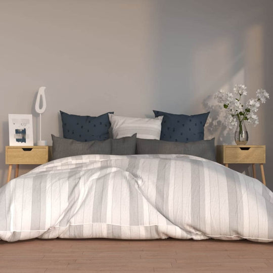 Bed with striped bedding, bedside cabinets, pillows, lamp, and flowers in modern bedroom decor.