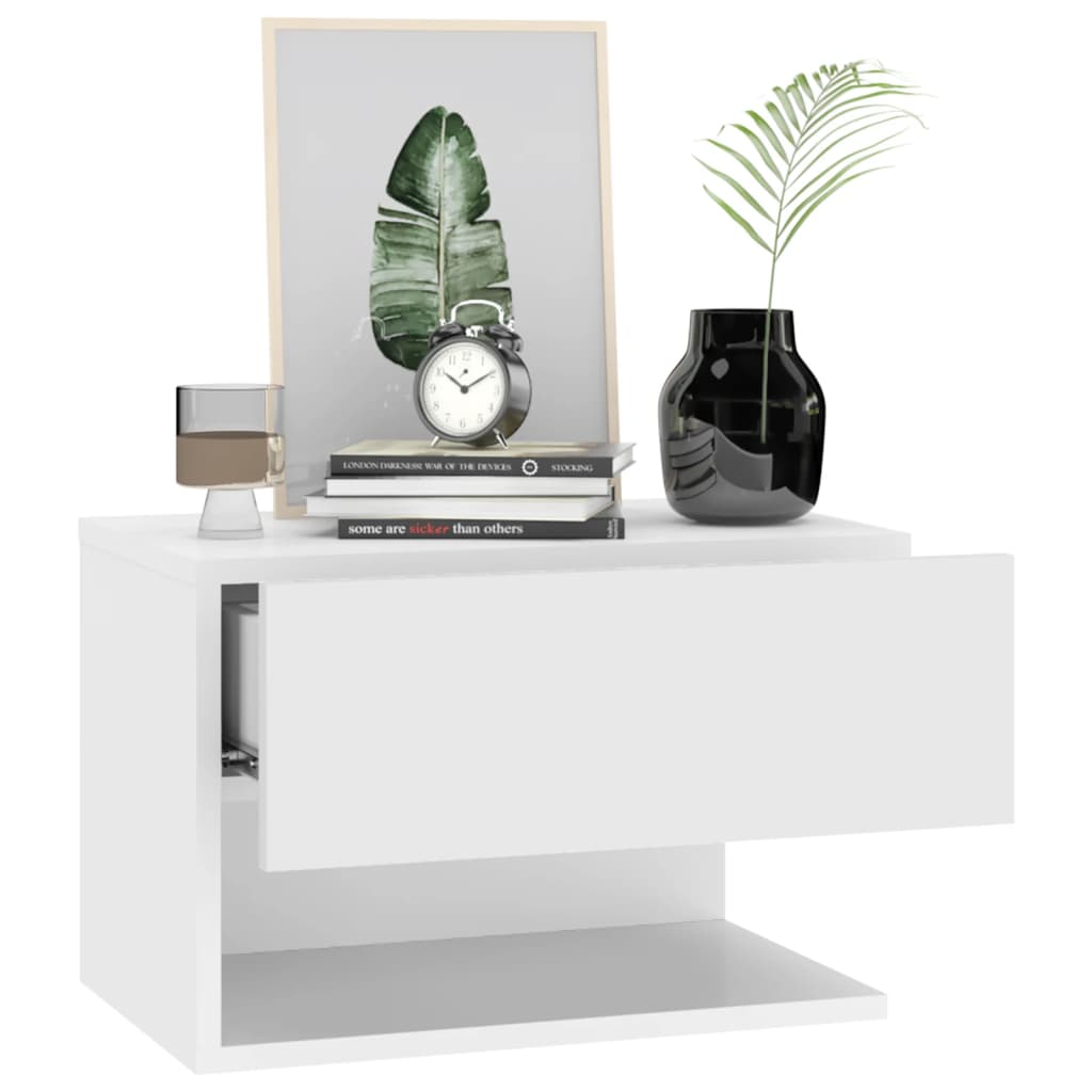 Wall-mounted white bedside cabinet with books, a clock, a black vase, and a framed leaf print on top.