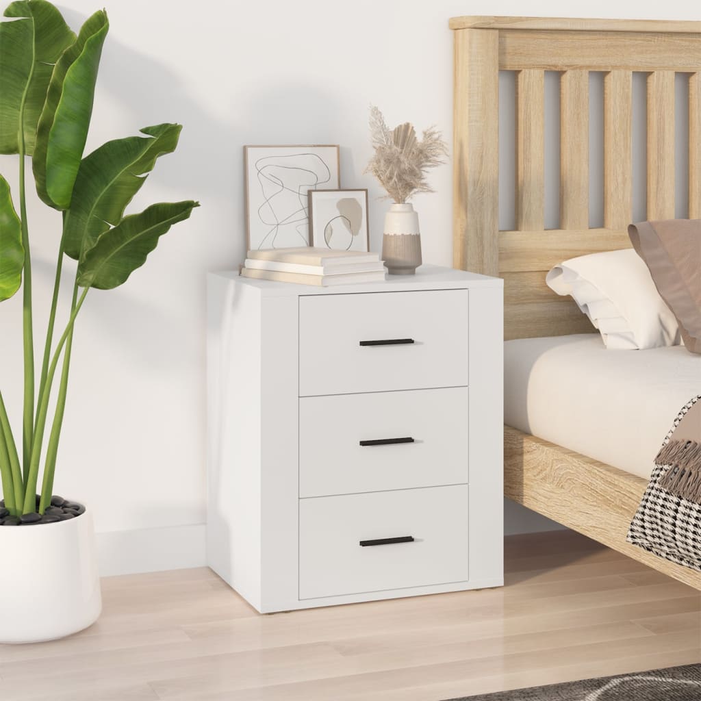 White engineered wood bedside cabinet with 3 drawers, offering affordable and quality storage, next to a bed and a plant.