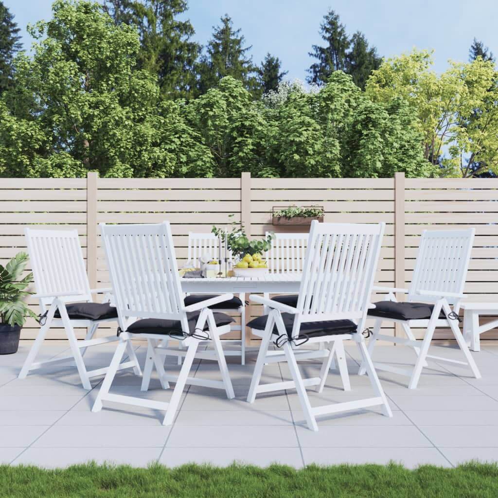 Outdoor dining set with white chairs featuring anthracite chair cushions on a patio with green foliage background.