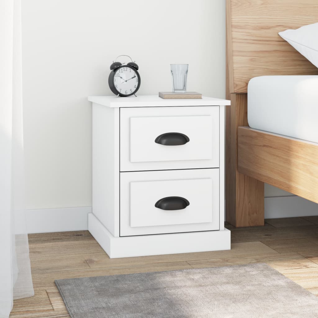 White bedside cabinet with 2 drawers made of engineered wood, placed next to a bed, featuring a clock and glass on top.