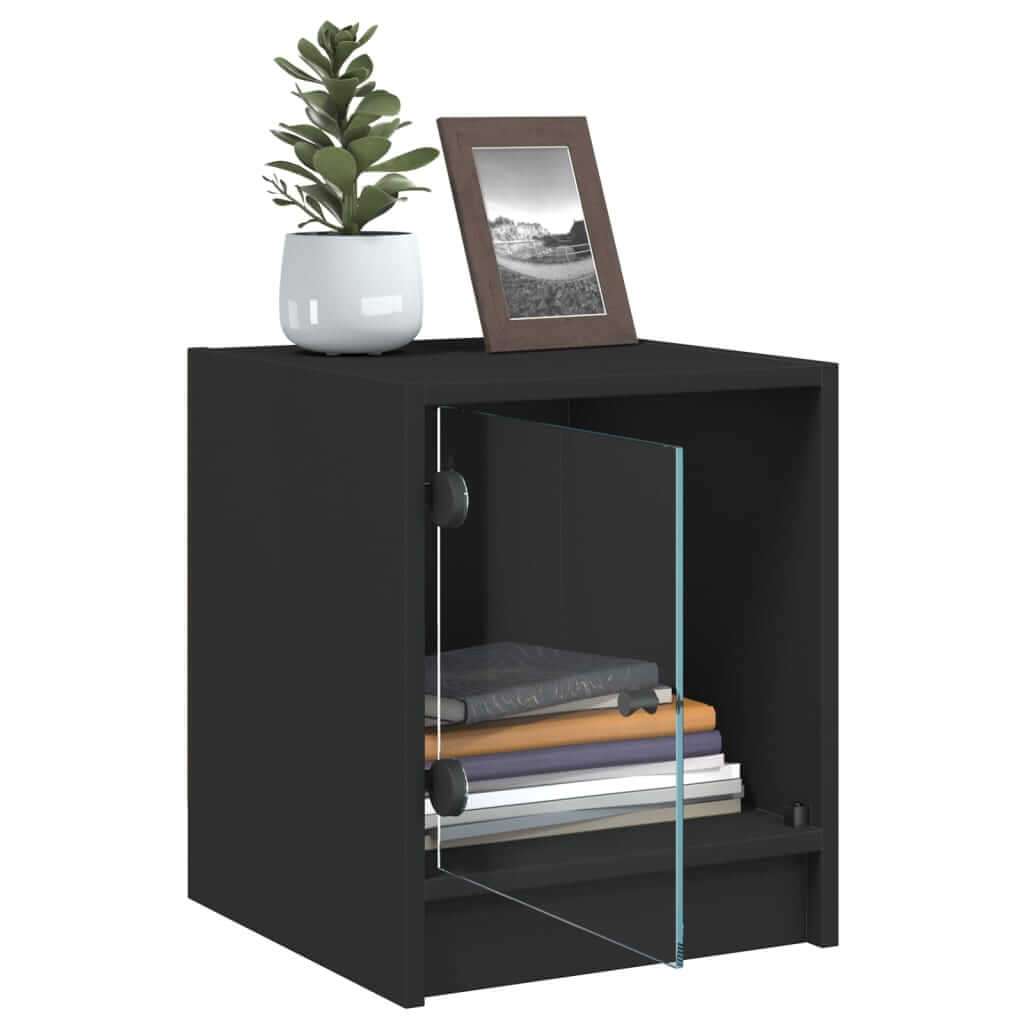 Black bedside cabinet with glass door, featuring a plant and photo frame on top and ample storage for books and small items. Affordable and quality.